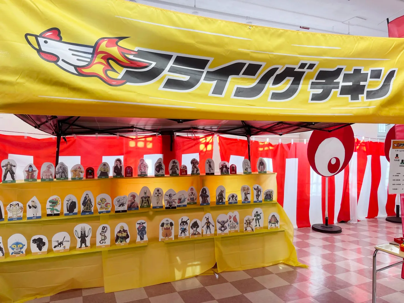 The Flying Chicken booth in operation with a yellow game sign, prize display, and festival decorations